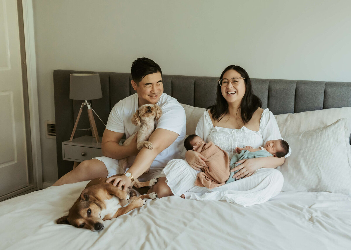 New parents to twins and laughing while sitting on their bed in their Sydney home with their two dogs.