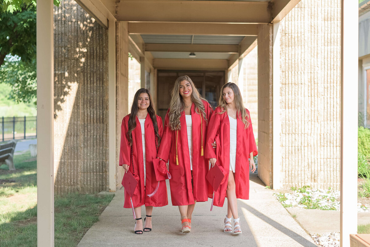 three high school senior girls  walking towards the camera with a red graduation gown
