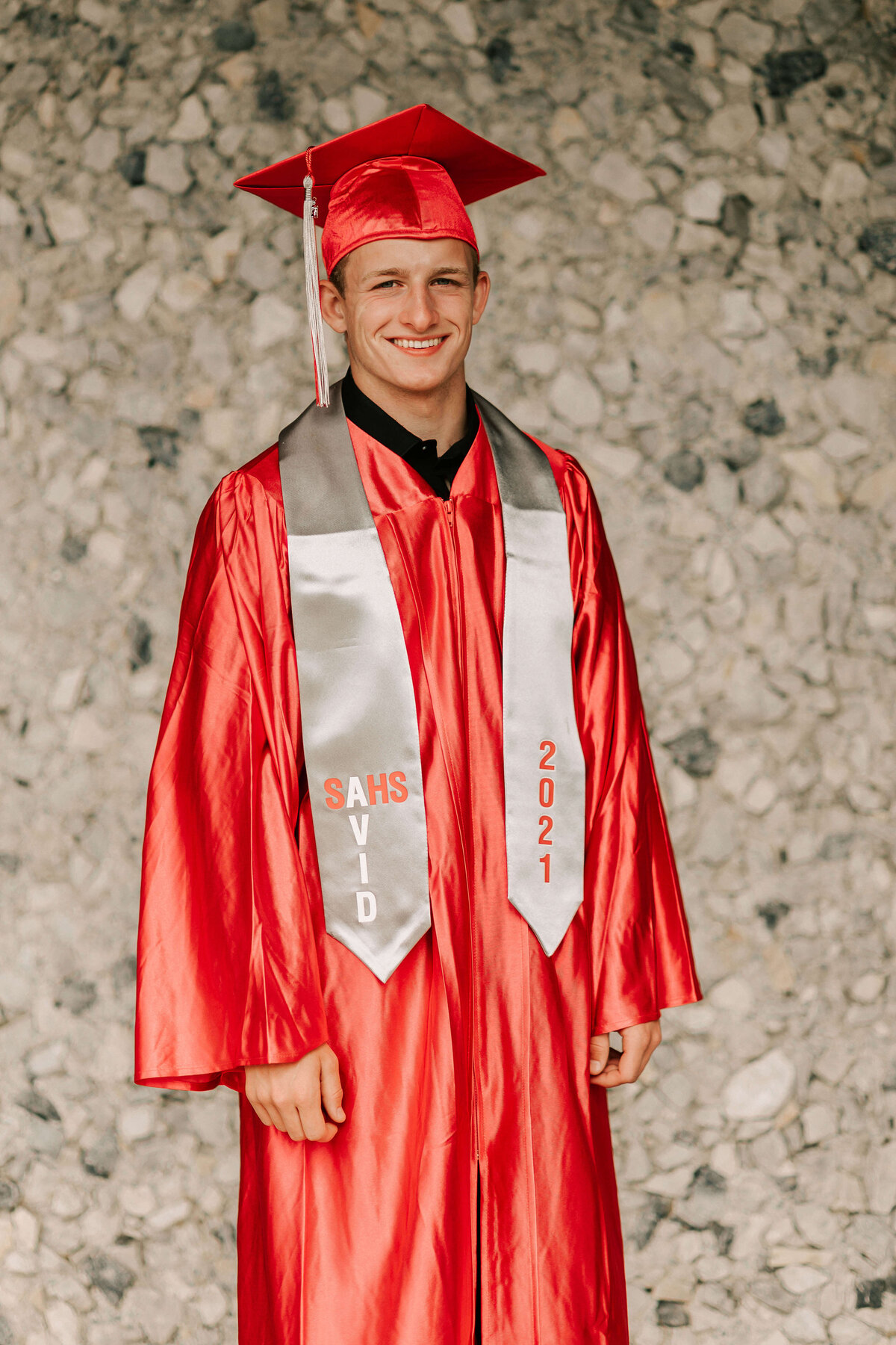 A high school senior in red and cap and gown stands in front of South Albany High School