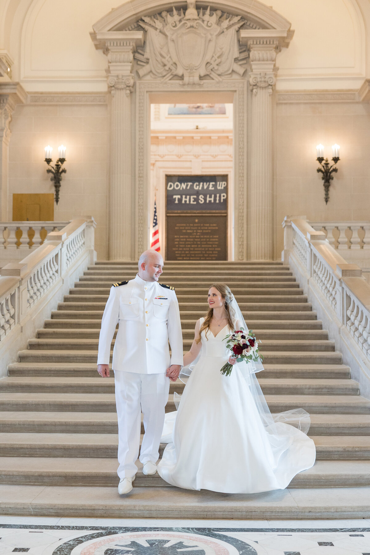 Naval Academy wedding in Annapolis, Maryland photo of bride and groom on step at Bancroft Memorial Hall with Don't Give Up The Ship sign by Christa Rae Photography