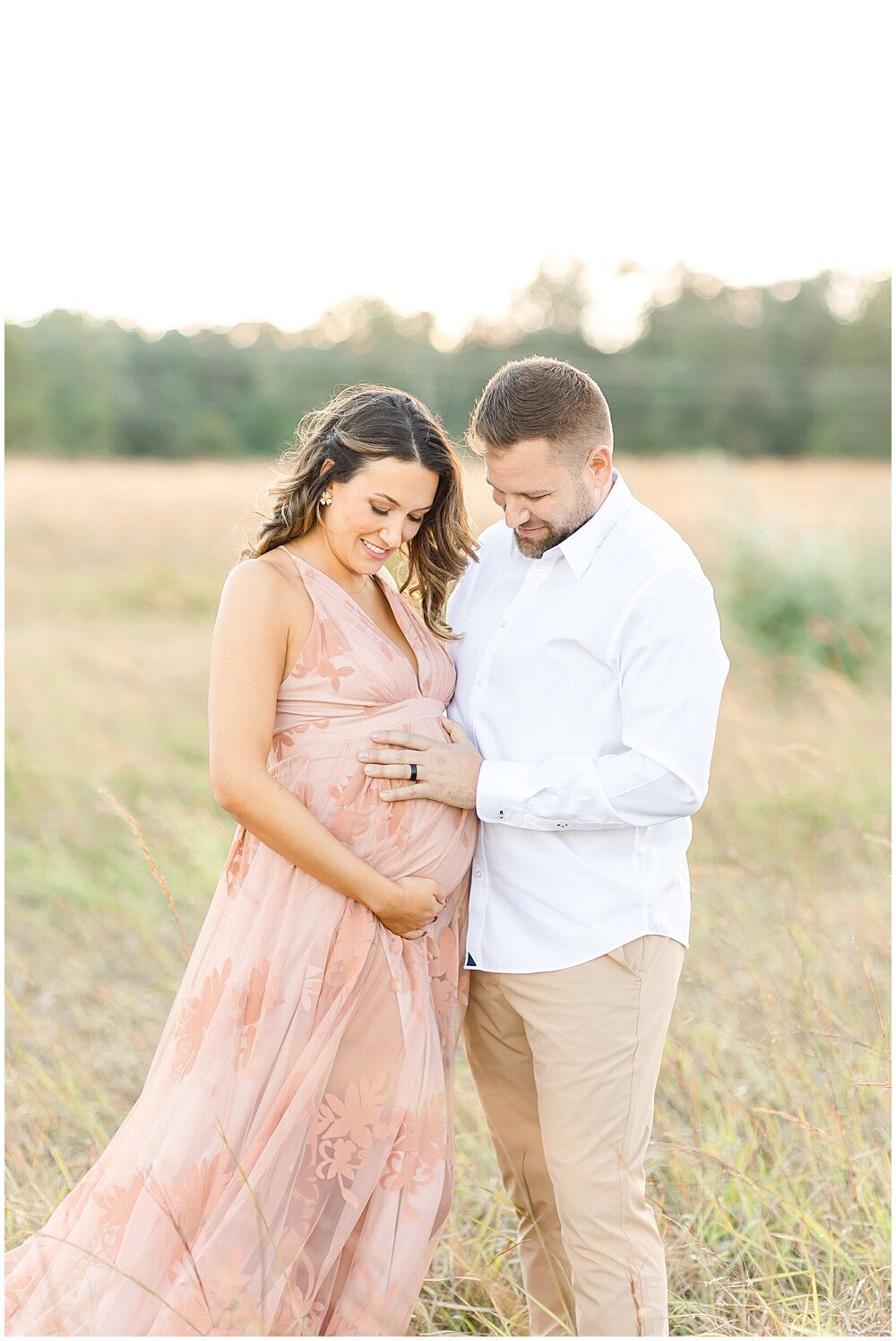 An expecting couple holding their baby bump in a field at sunset by northern virginia newborn photographer