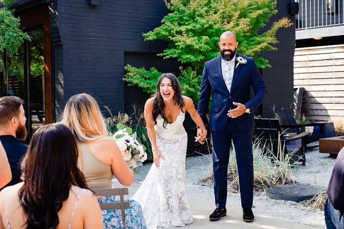 Bride in strapless lace dress laughs outside of BODE Nashville as she holds the groom's hand at their elopement wedding