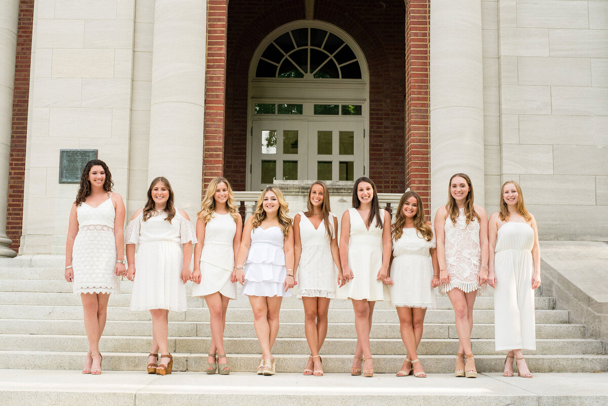 Senior girls holding hands and wearing white dresses smiling at the camera and looking at the camera