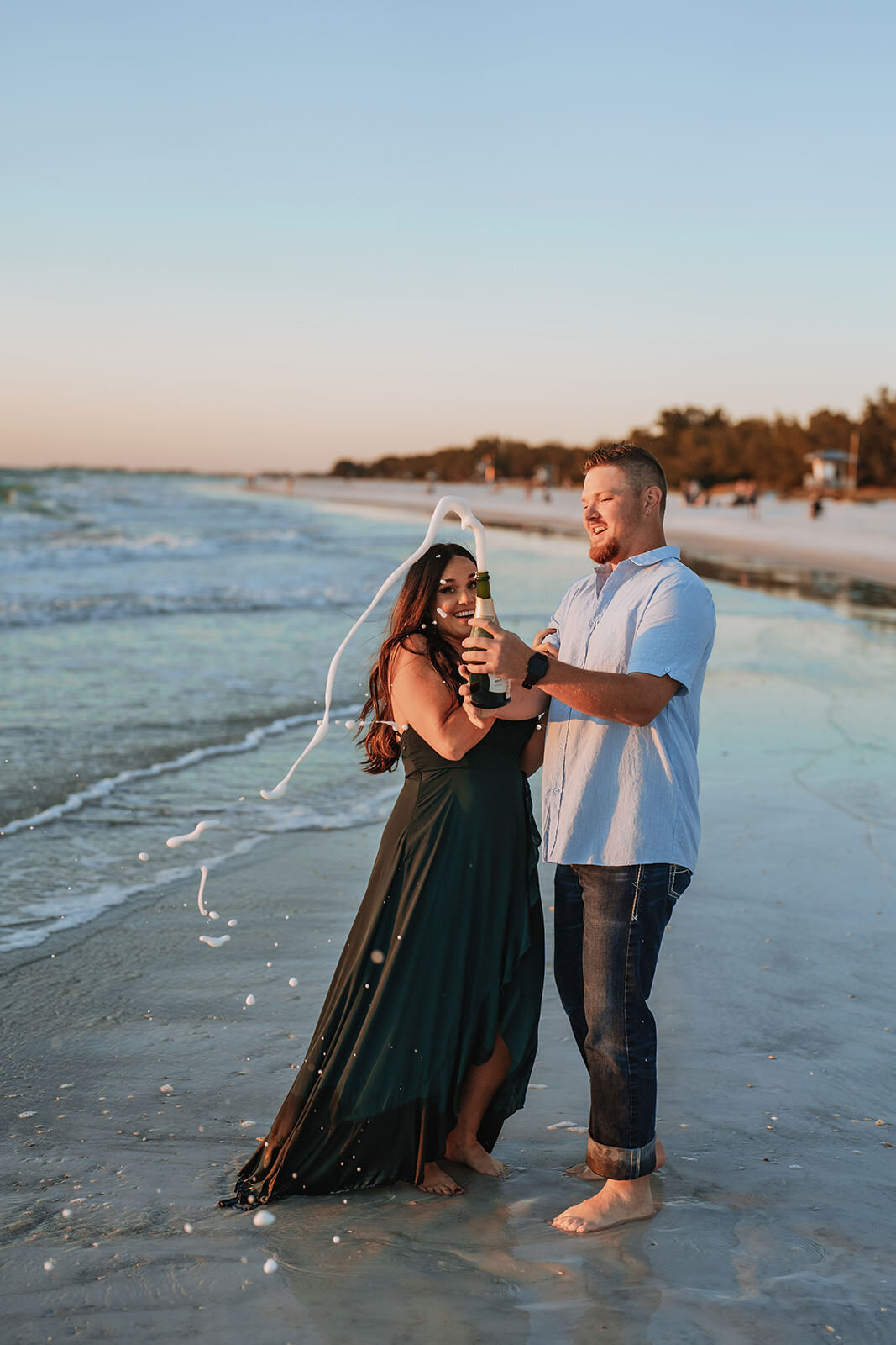 couple popping champagne on coquina beach during engagement session