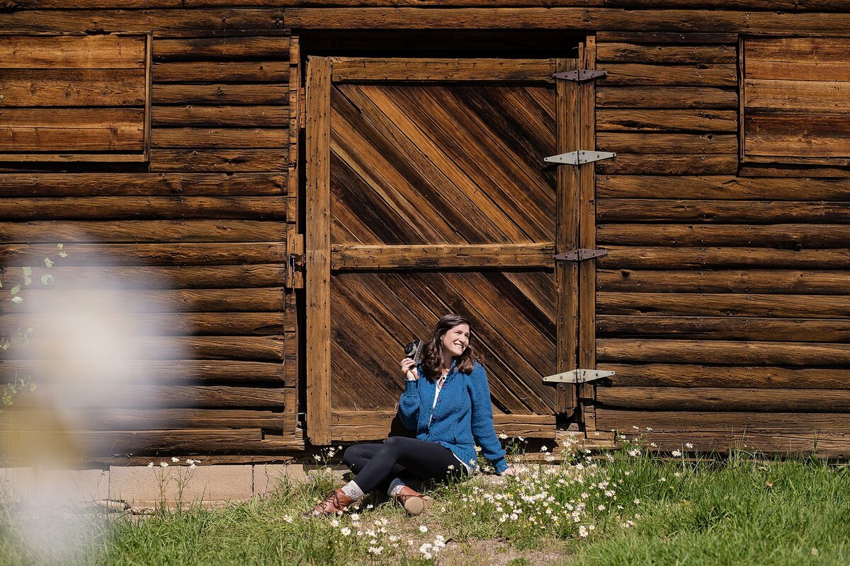 woman in blue sweater holding camera in front of wooden door