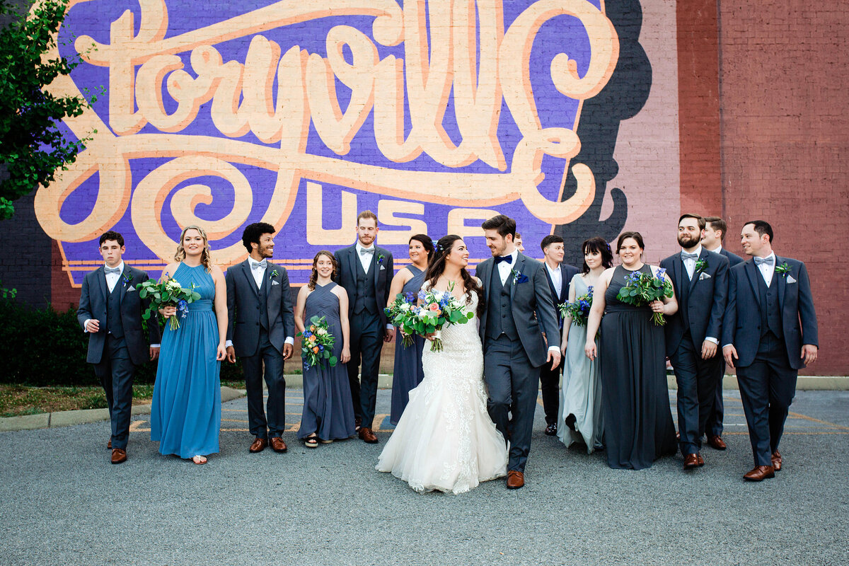 Bridal party walking with couple outside Cannery ONE in Nashville with the Storyville USA mural behind them
