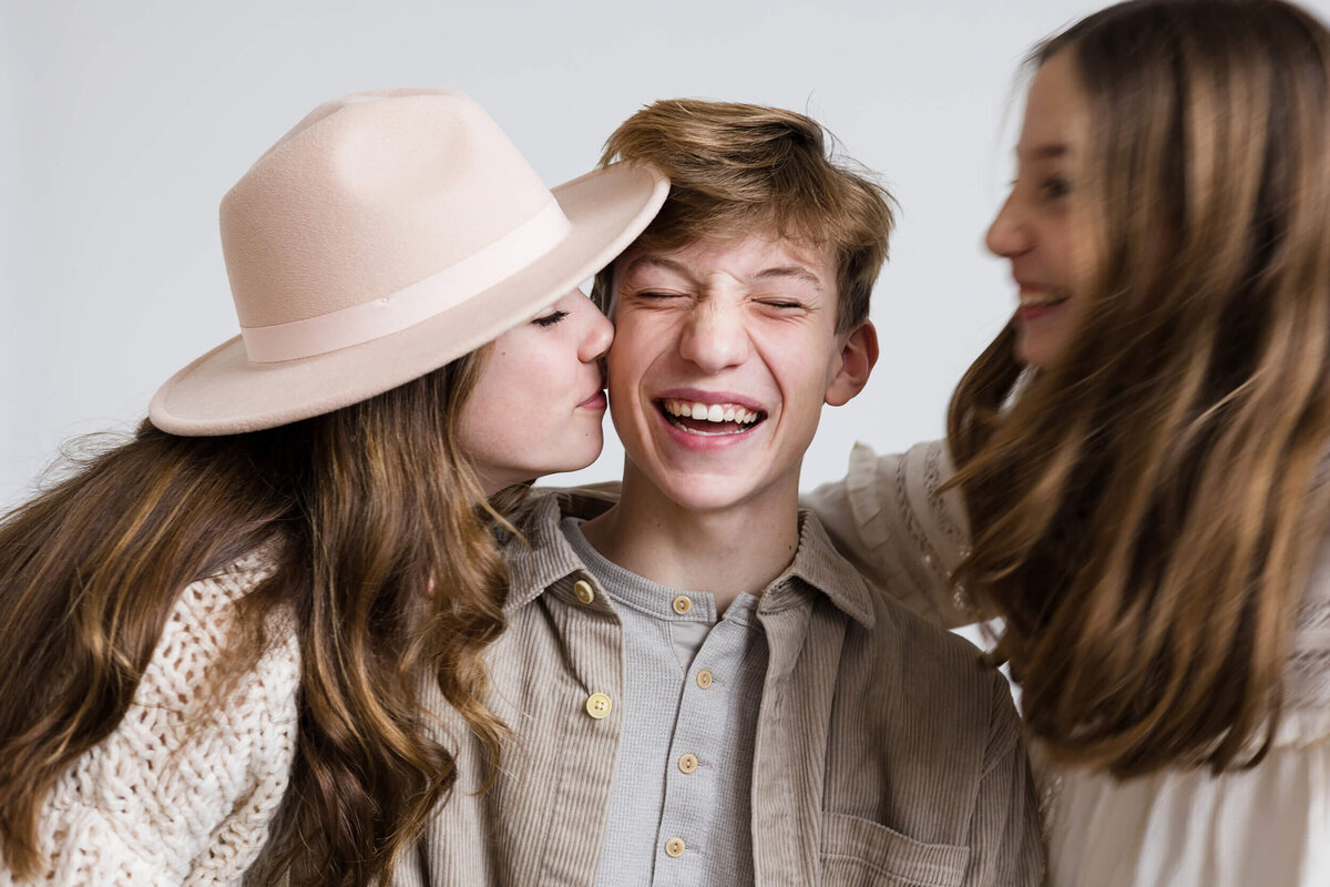 Sisters kiss brother in  photography studio for a mn family photographer
