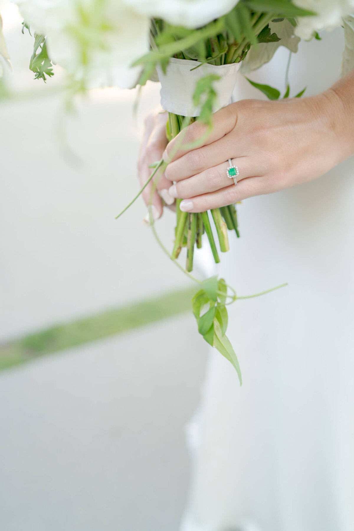 Bride's hands in an emerald ring holds a bouquet of white flowers.