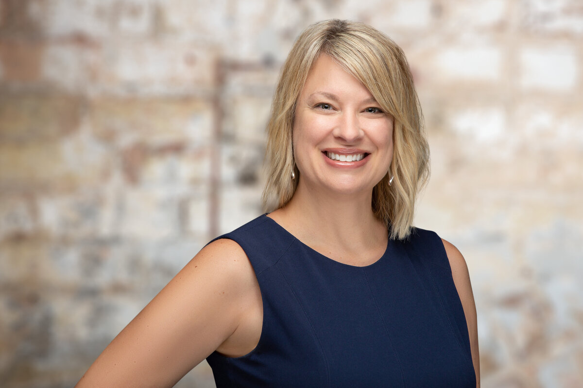 A blonde woman real mortgage professional poses for a headshot on a brick background at Janel Lee Photography studios in Cincinnati Ohio