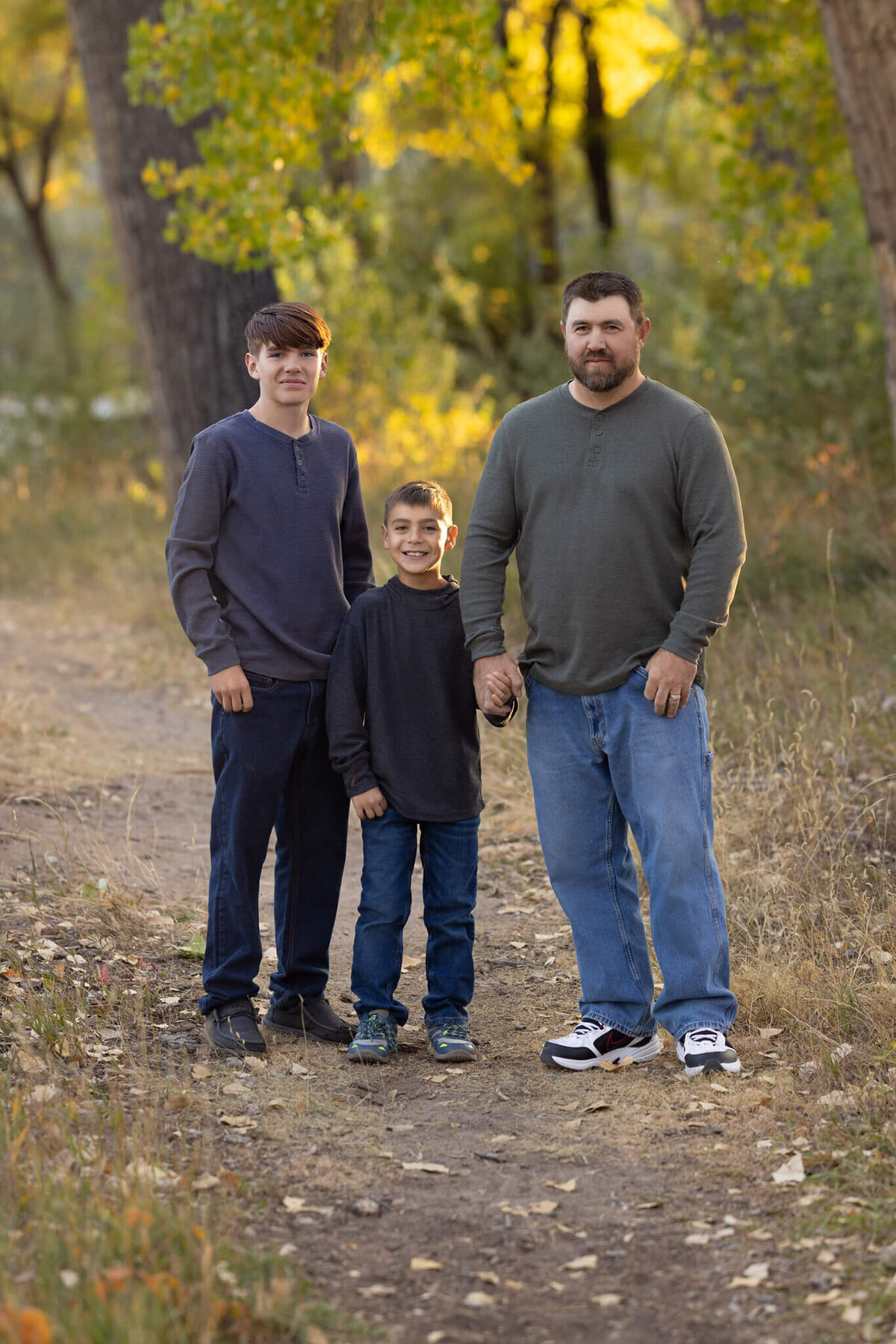 a dad and his two sons standing on a trail in a forest
