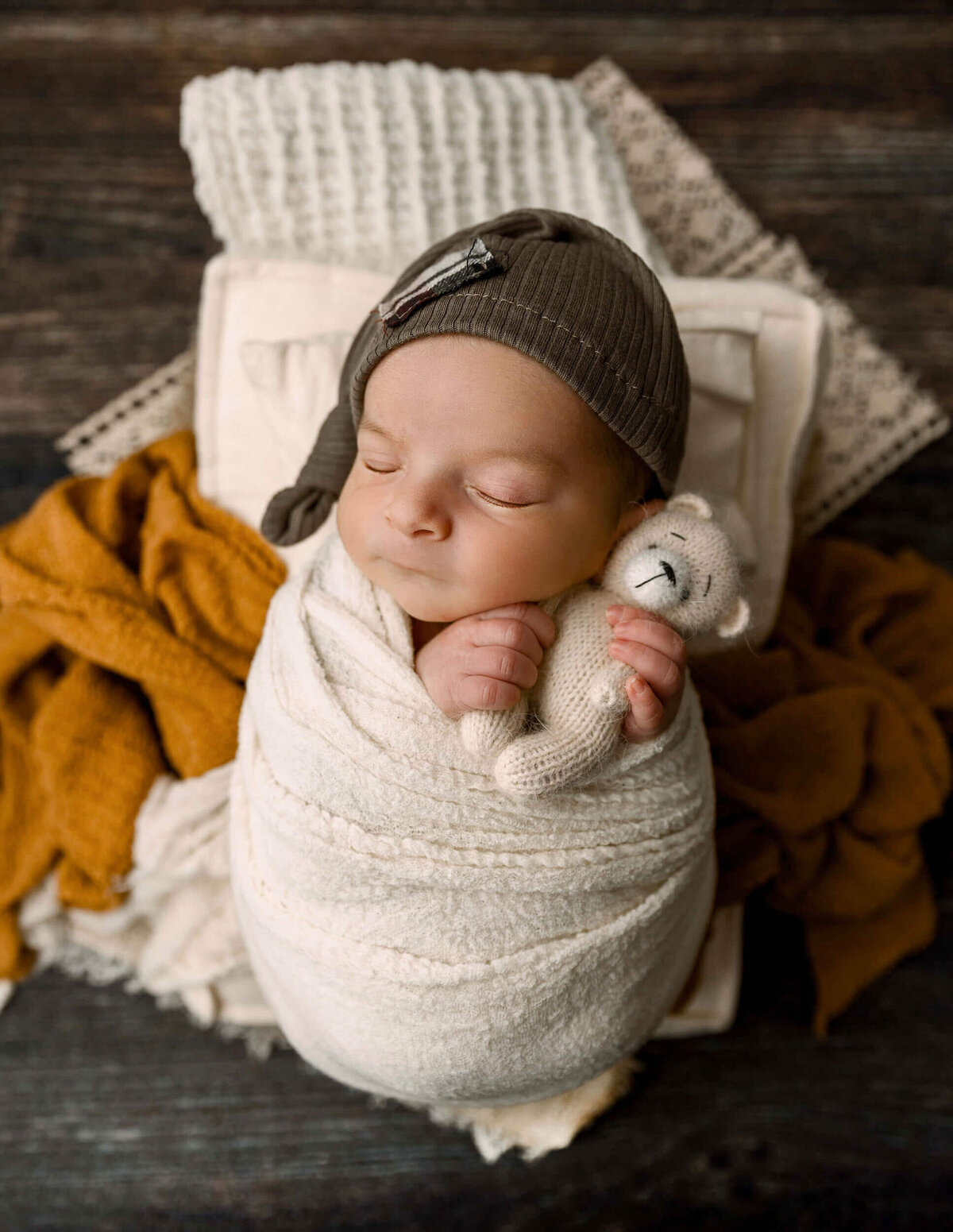 Newborn baby boy in a wrapped pose holding a teddy bear with a sleepy cap in an Erie photography studio