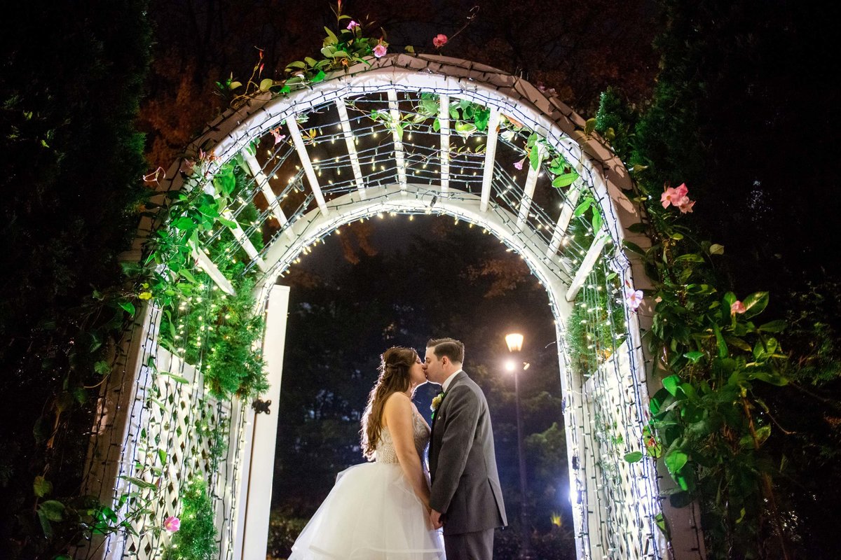 Bride and groom kissing at night under the arch at Fox Hollow