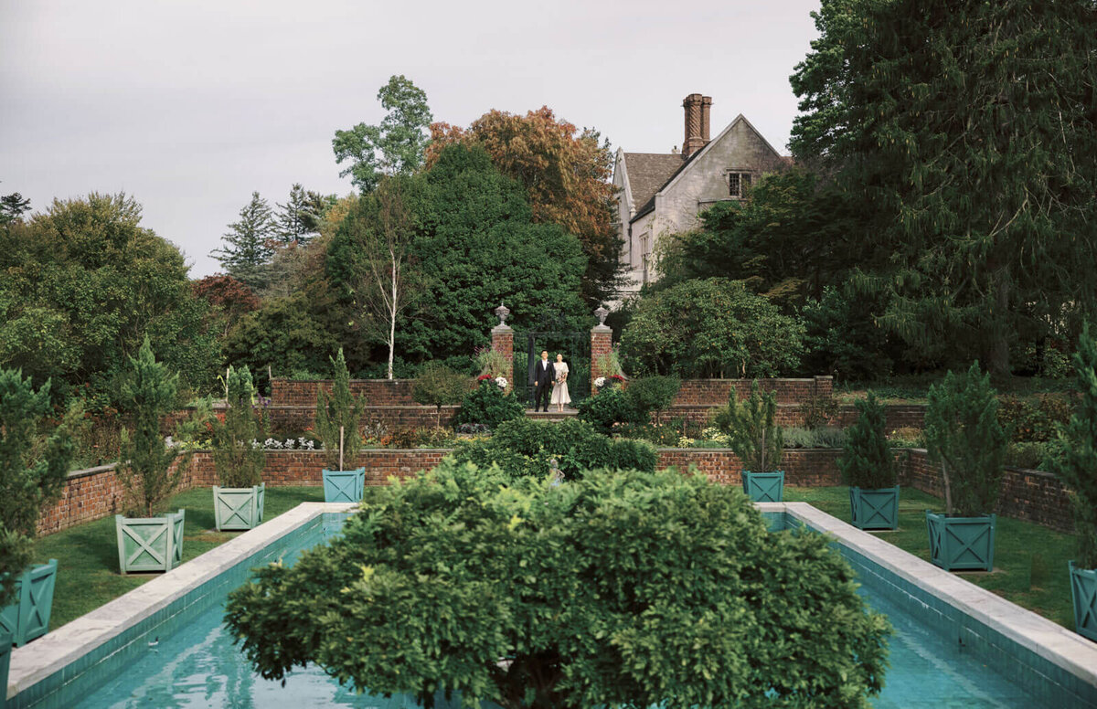 The engaged couple is amidst lush greenery and a swimming pool at Planting Fields Arboretum, NY. Image by Jenny Fu Studio