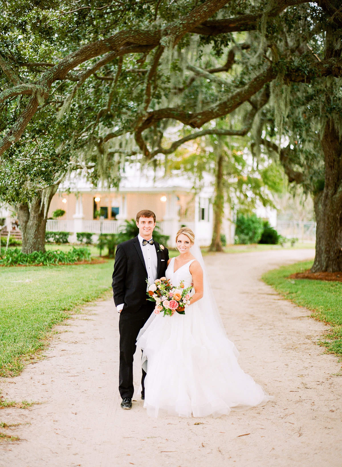 Classic Charleston Newlyweds Stand in front Classic White Plantation House under Spanish Moss Live Oaks Trees