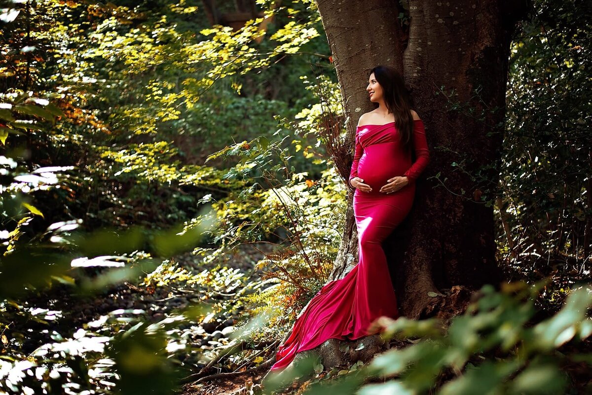 Outdoor maternity session in Burnaby with pregnant woman in magenta pink gown surrounded by foliage