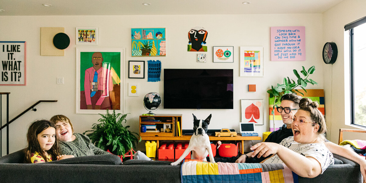 mother, father, and young daughters laughing on the sofa with their pet dog during an in-home family session in san francisco.