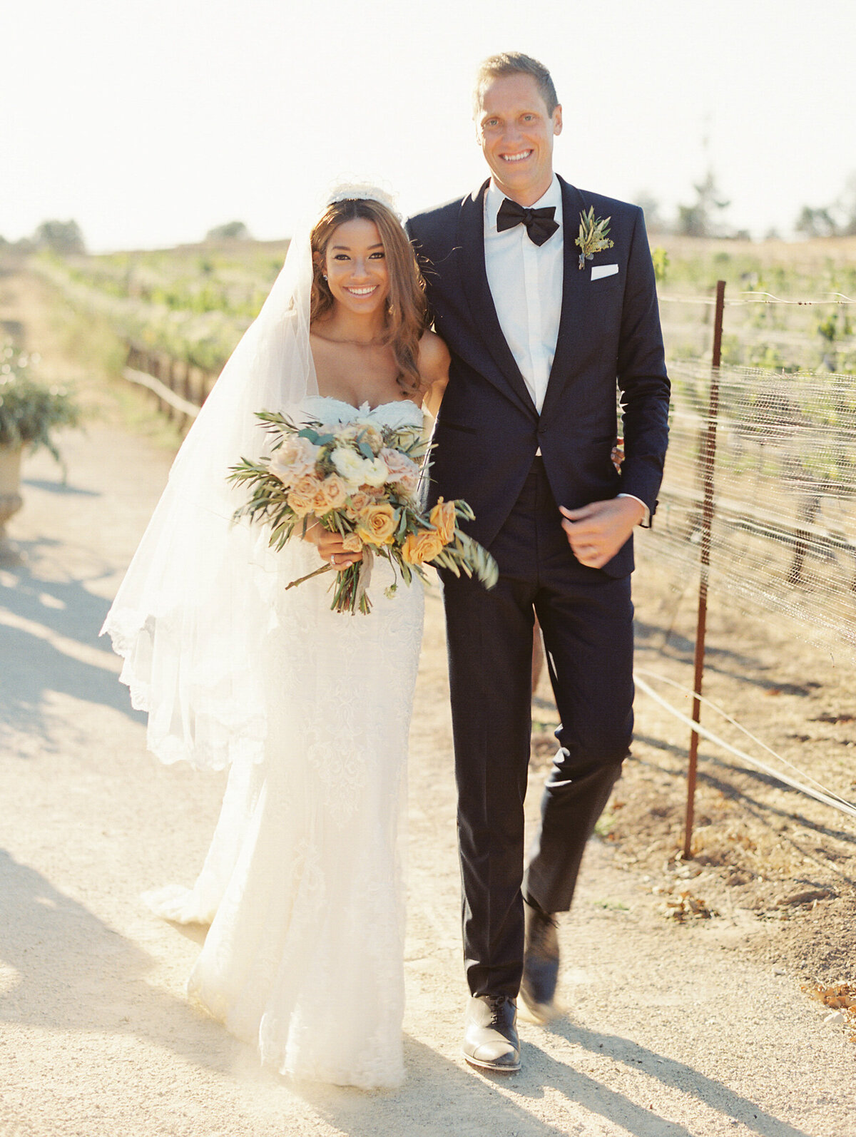 couple walking through a vineyard just after saying I do