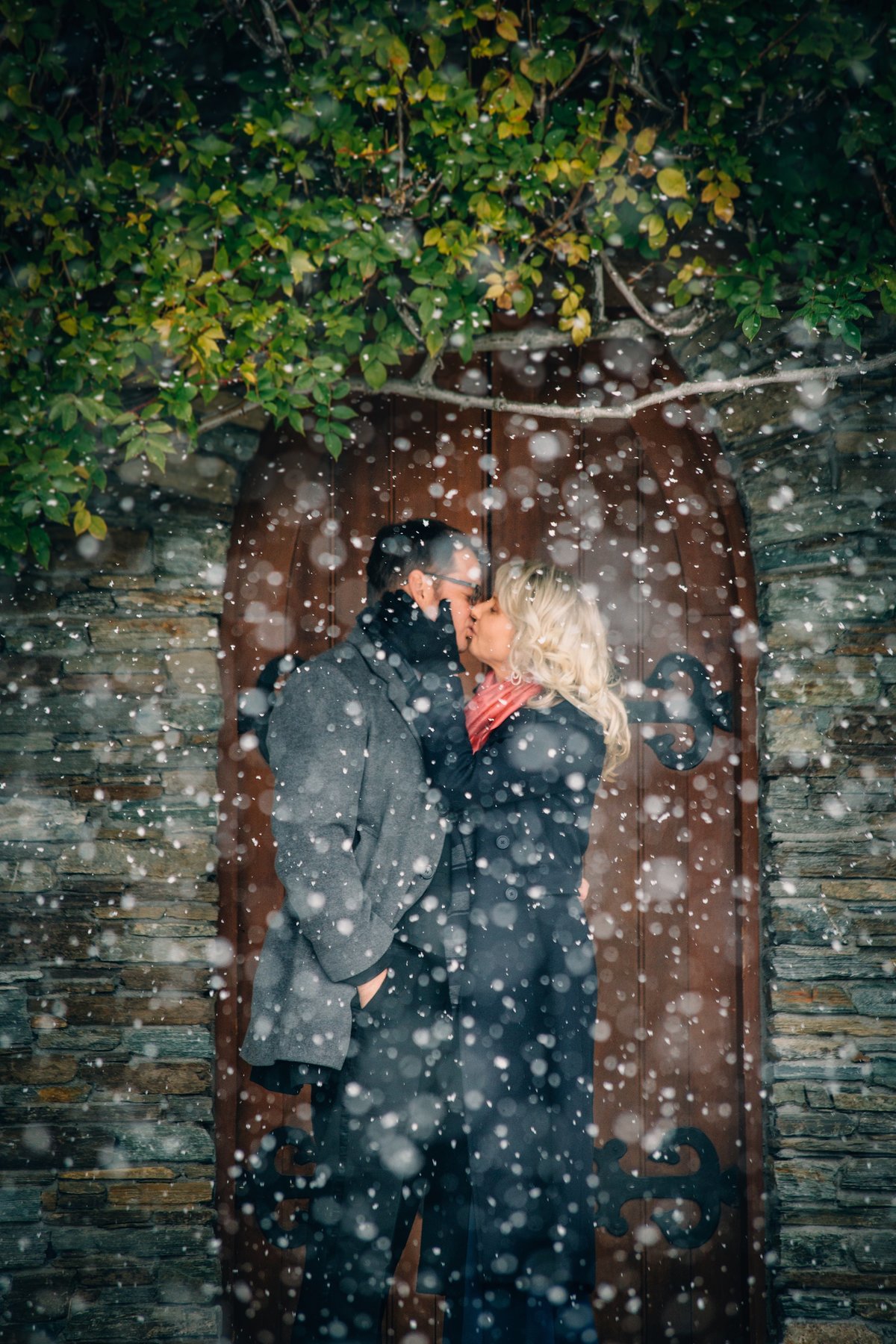 Bride and groom kissing in the snow in front of an old chapel