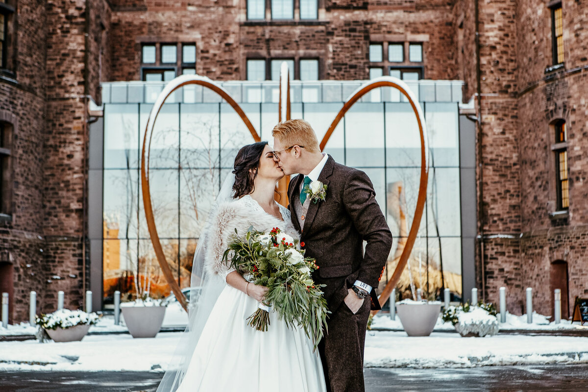Winter wedding with bride and groom kissing outside in front of Hotel Henry in Buffalo, New York