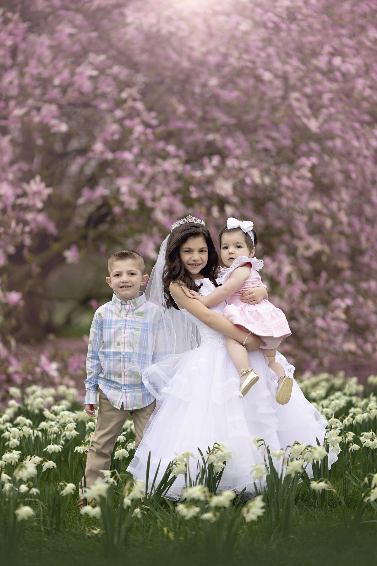 Three sibling stand in wildflowers in front of pink flowering trees