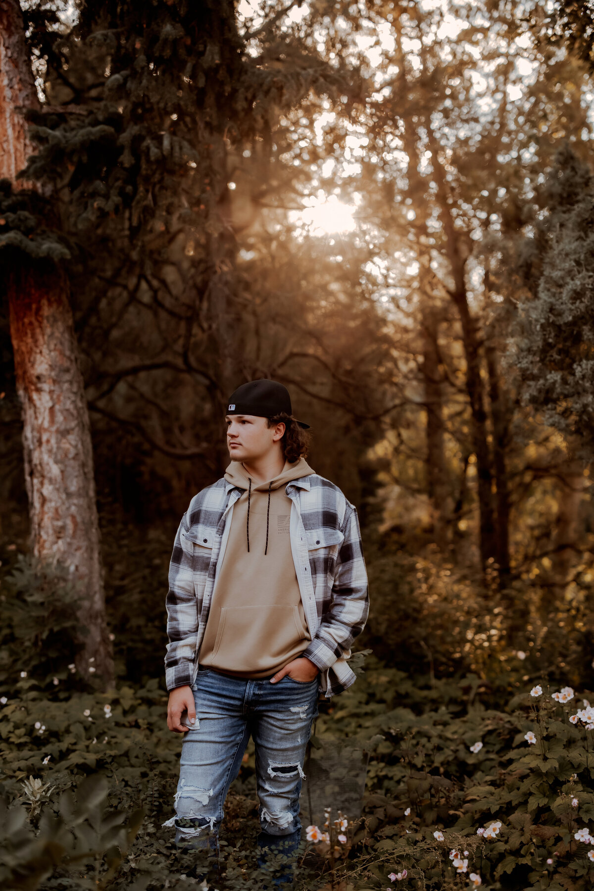 senior boy stands in trees and flowers at golden hour in boulder colorado