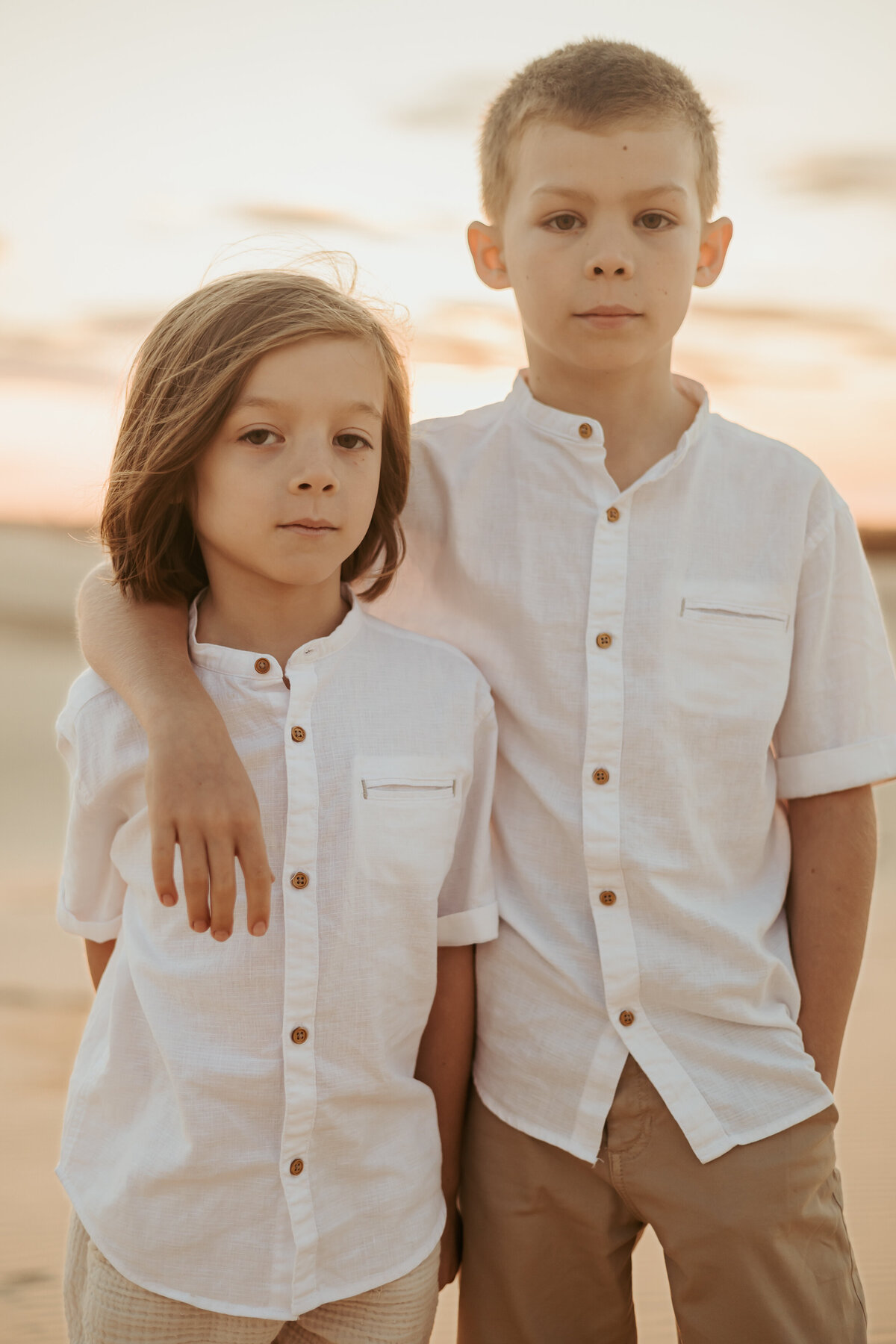 A young boy has his arm around his younger brother as they stare directly into the camera for their photoshoot.
