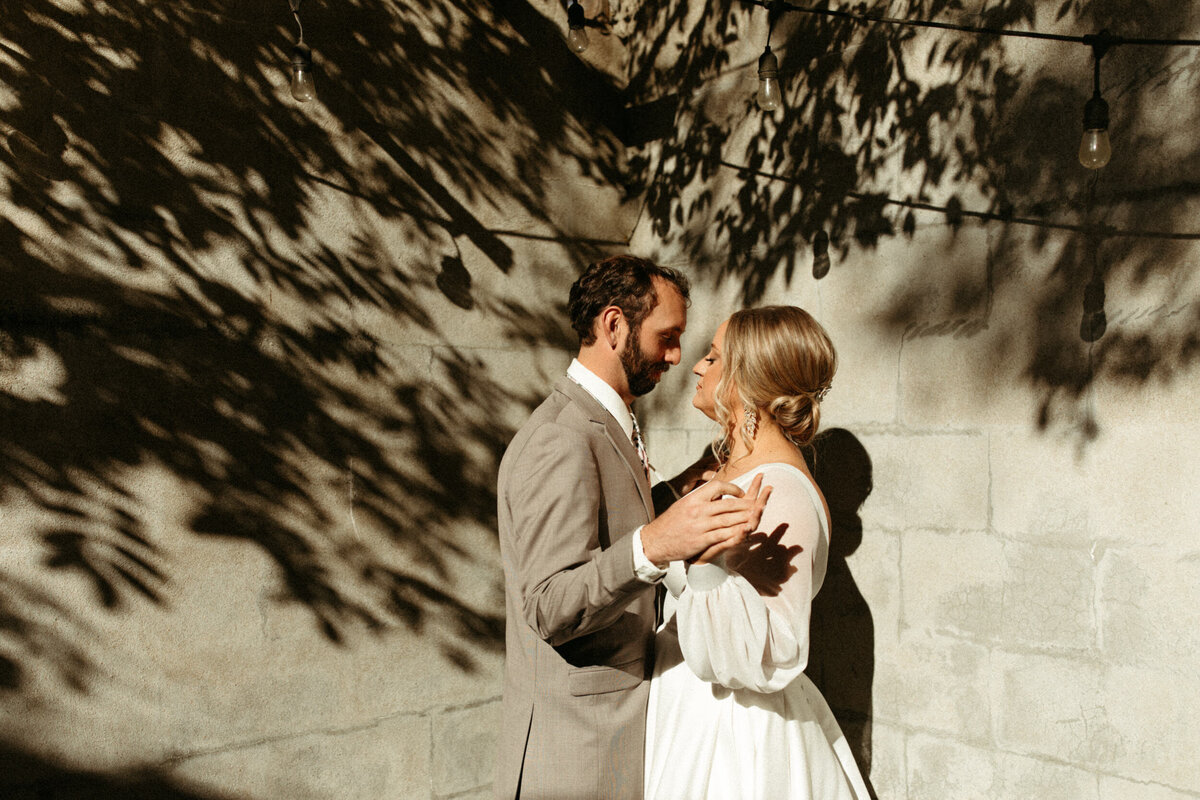 Bride and groom holding hands and looking at each other in harsh lighting with shadows around them