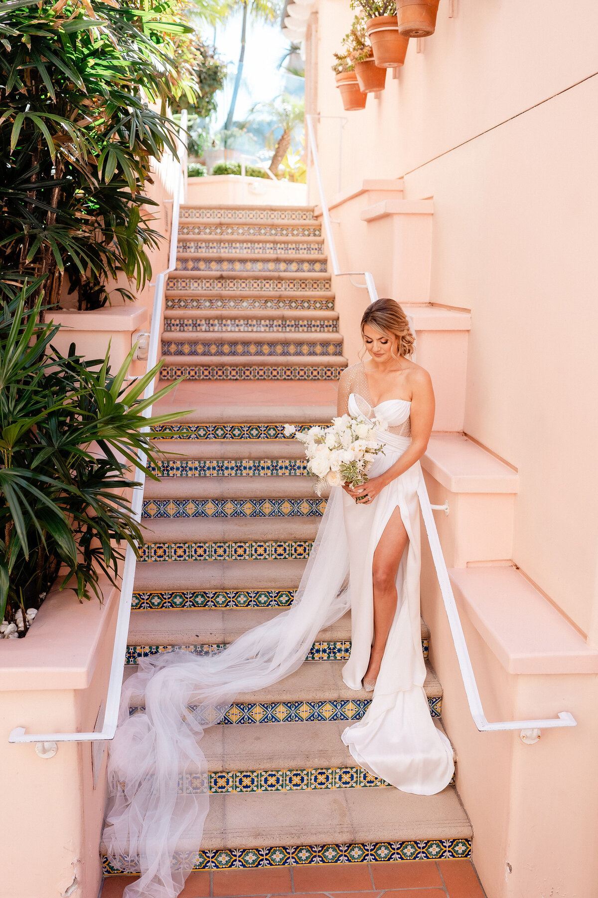 Beautiful old Hollywood style meets Spanish details.  The bride is standing on the stairs looking at her white bouquet against the spanish tiles.