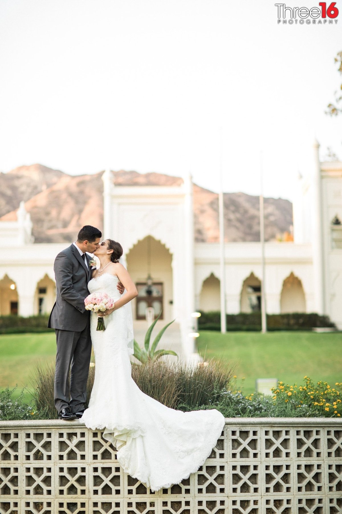 Bride and Groom share a kiss while standing on a short wall at the Brand Library Park