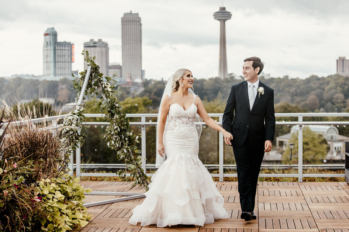 Bride and Groom holding hands with city backdrop in Niagara Falls State Park, NY