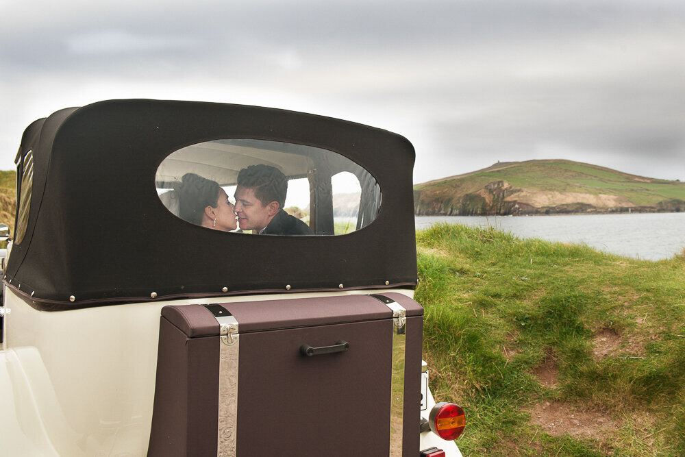 bride and groom kissing in a vintage, soft top  car while parked at Bin Ban beach in Kerry