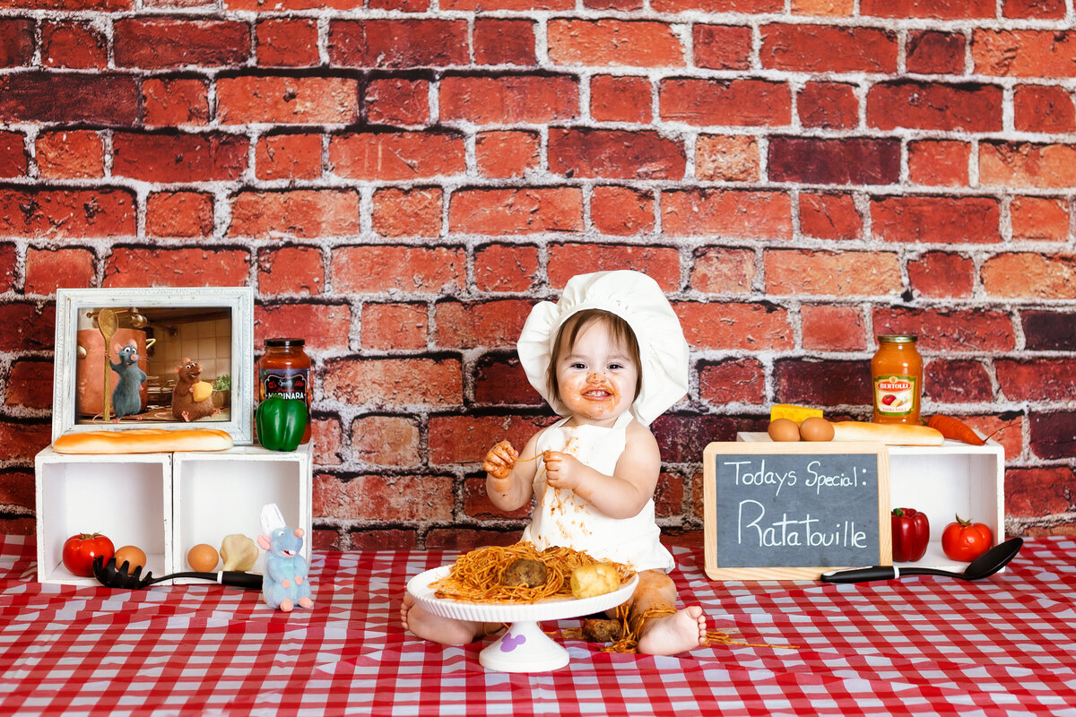 Cake Smash Photographer, a baby sits with a plate of spaghetti and meatballs, dressed as a chef, and before a restaurant style backdrop