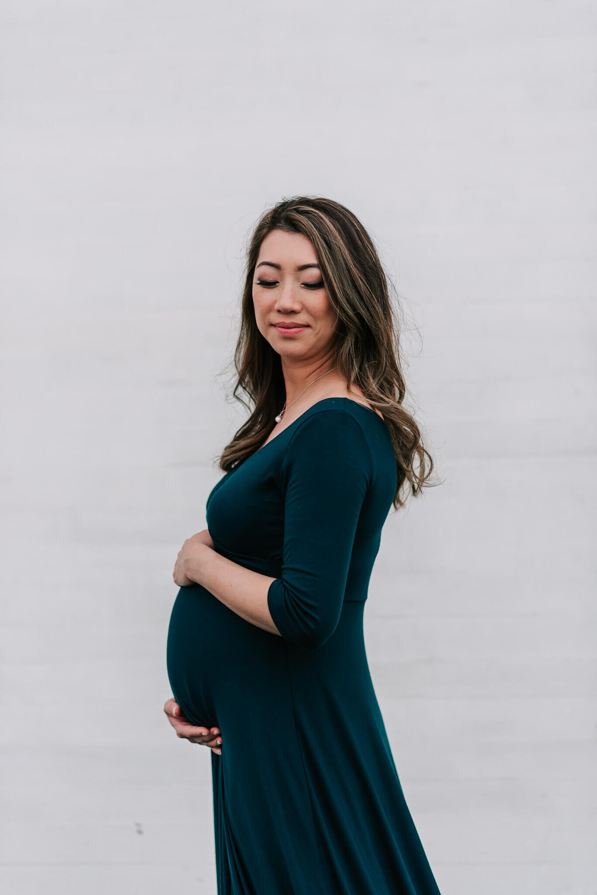A glowing mama holding her belly against a white wall, by a northern Virginia maternity photographer