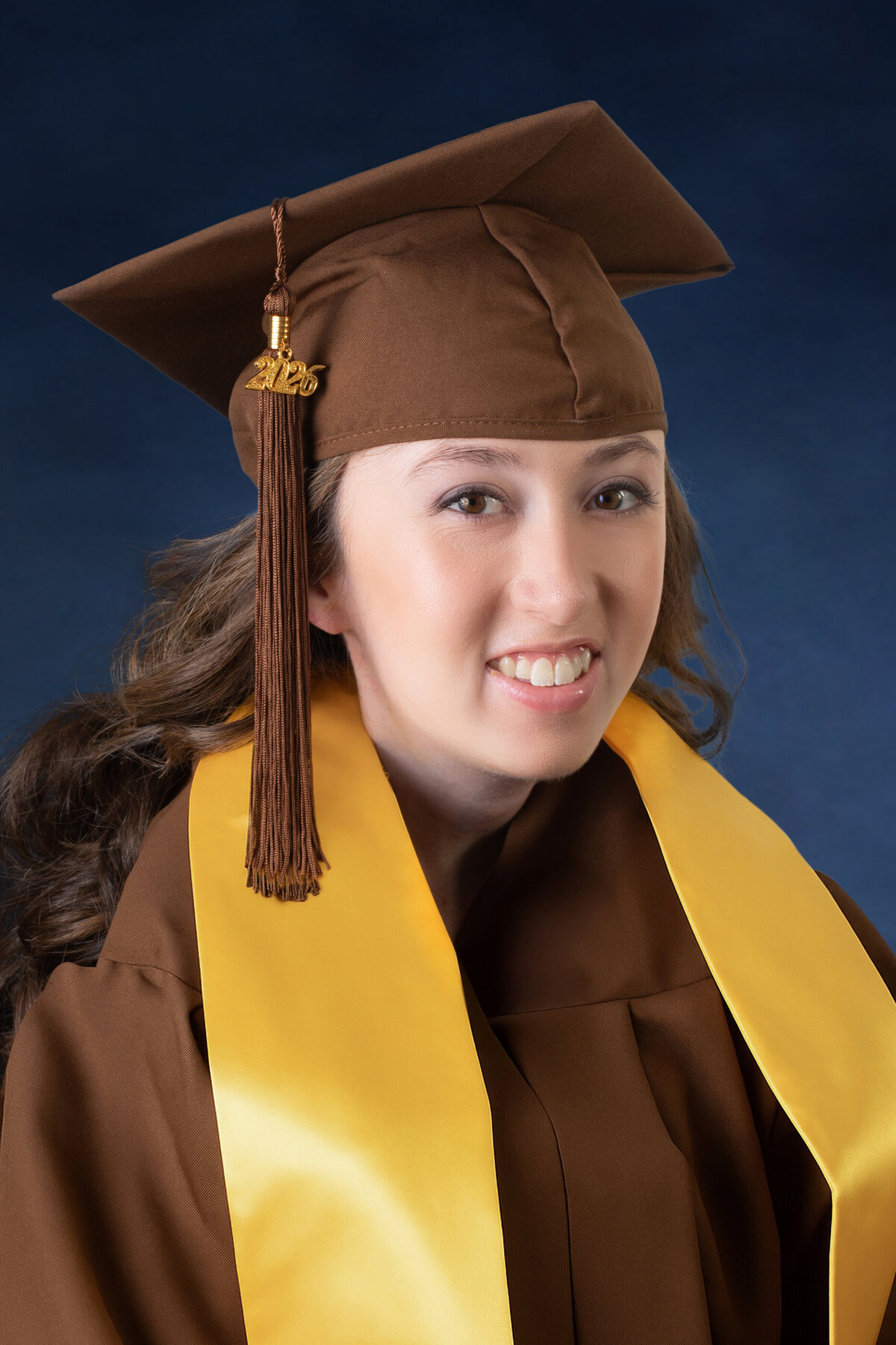 white teenage girl with brown hair twirls wears a brown graduation cap and gown  Clarkstown South senior portrait photographer Milestone Images