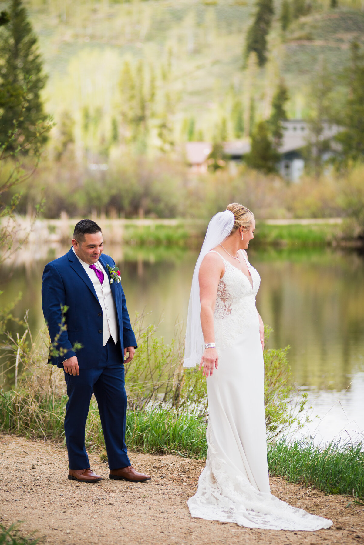 A groom checks out the back of his bride's dress in front of a pond during their first look.