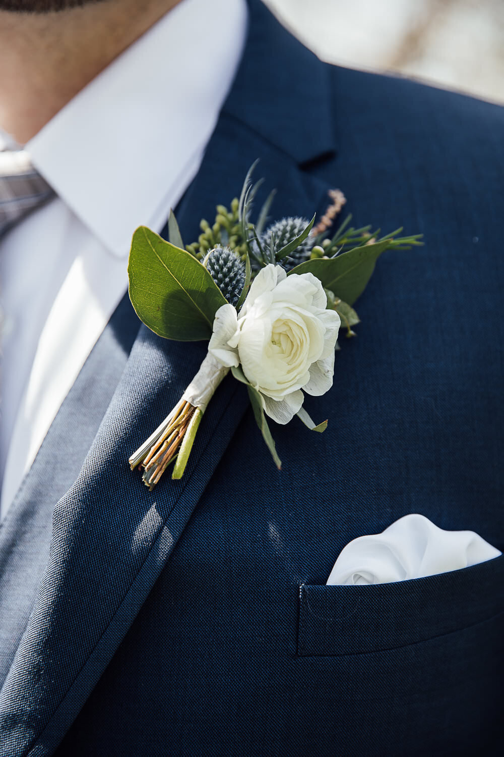 White ranunculus, blue thistle, and blush astilbe boutonniere