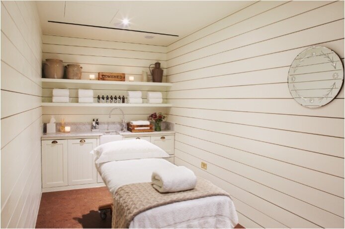 Vintage inspired spa treatment room with white wood board panelled wall, cork floor and white built in millwork and round vintage etched mirror