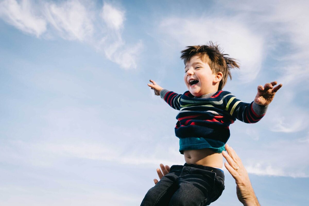 toddler boy being thrown in the air during a family photo session at baker beach in san francisco.