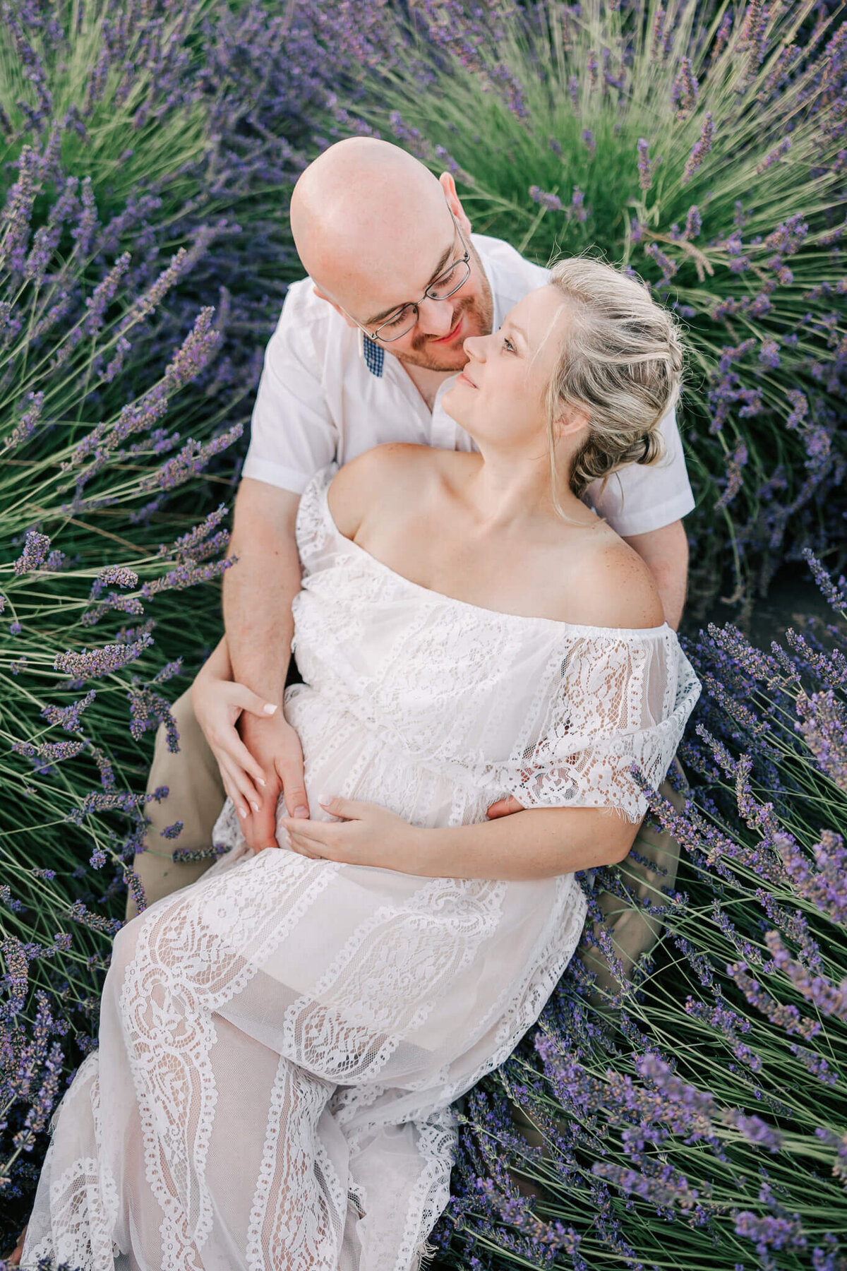 mom and dad with their hands on her belly laying down in lavender field