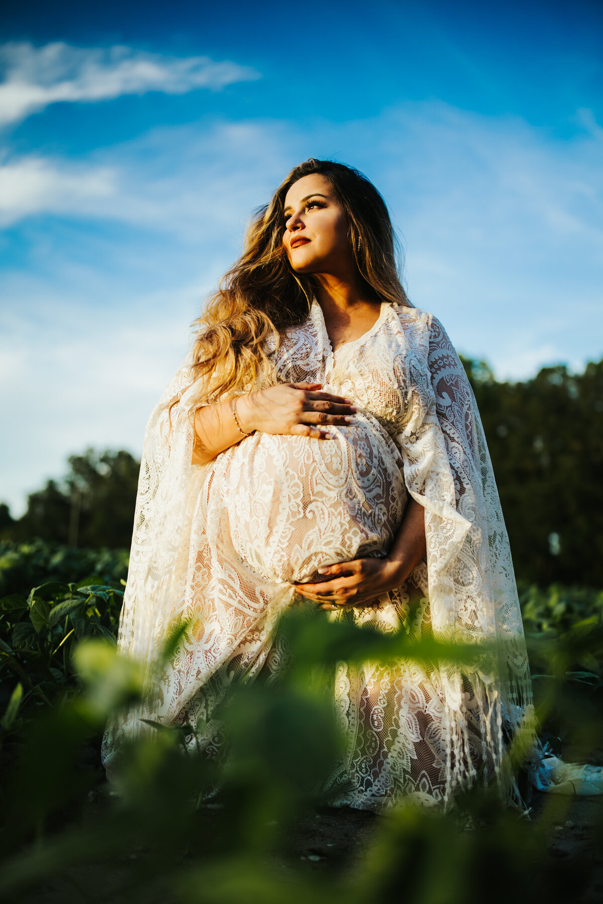 colorful harsh lit Maternity photo of a women in a lace dress sitting in a farm field