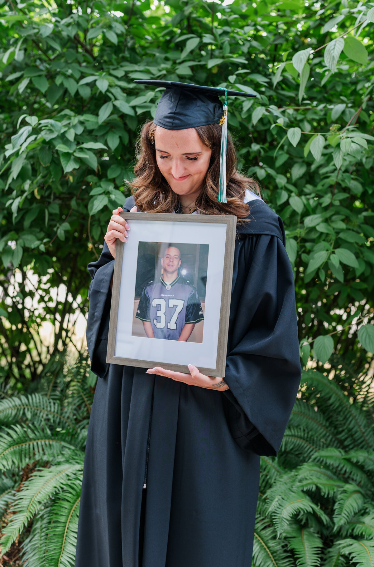 Graduation photo day grad student holds a frame of her brother in her hands looking down at the photo frame.