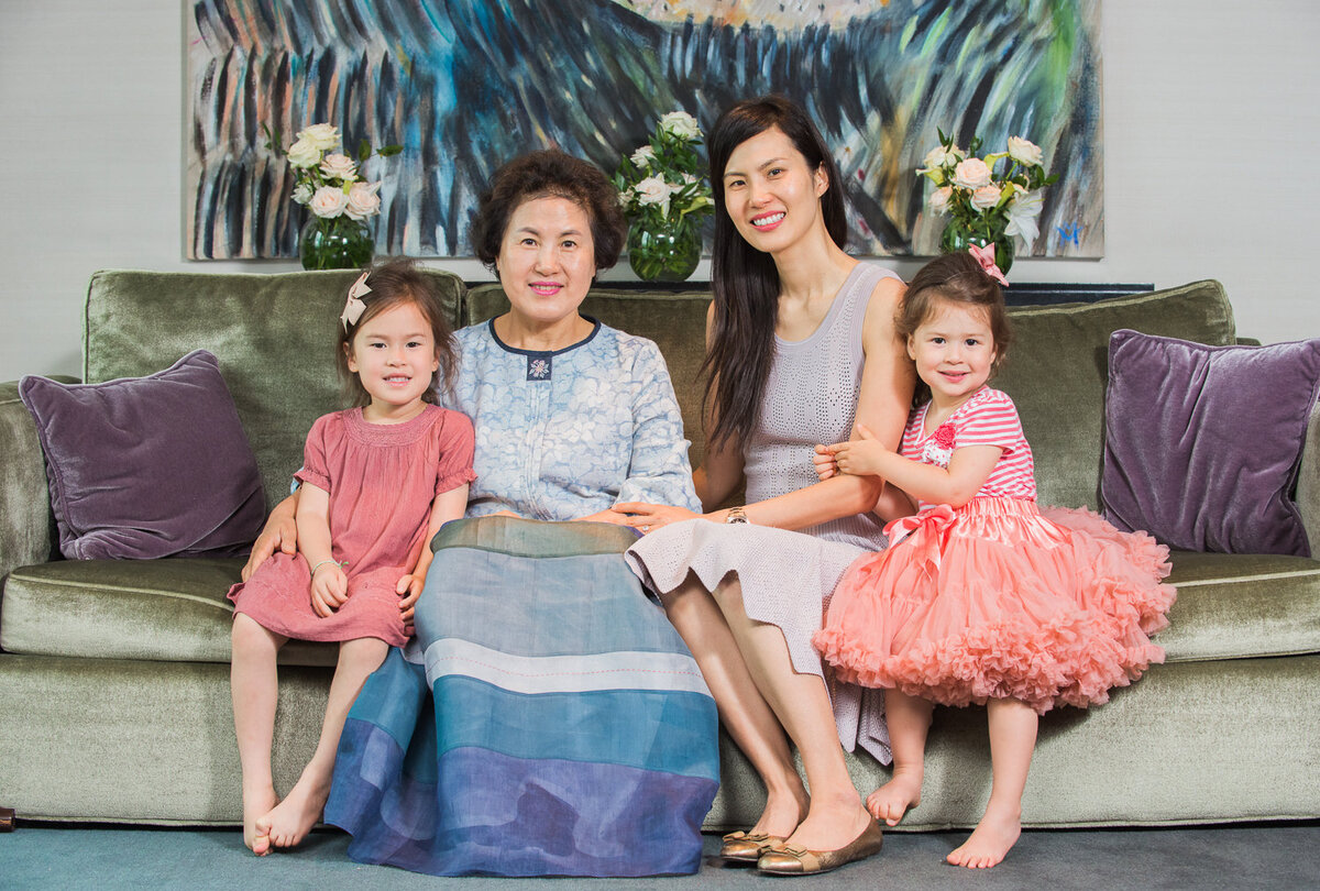 Portrait of an asian grandmother, daughter and grand daughters sitting on a grey sofa in colourful clothes