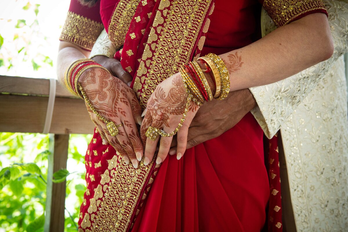 Close-up of a person in a traditional red and gold sari, adorned with gold bangles and showing detailed henna designs on their hands at an event in Davenport.