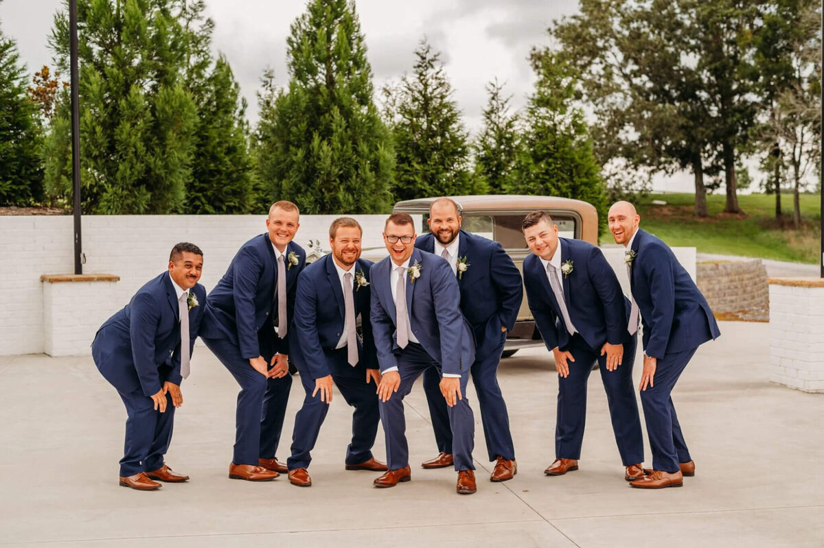 Photo of men wearing navy suits and squatting with silly faces outside