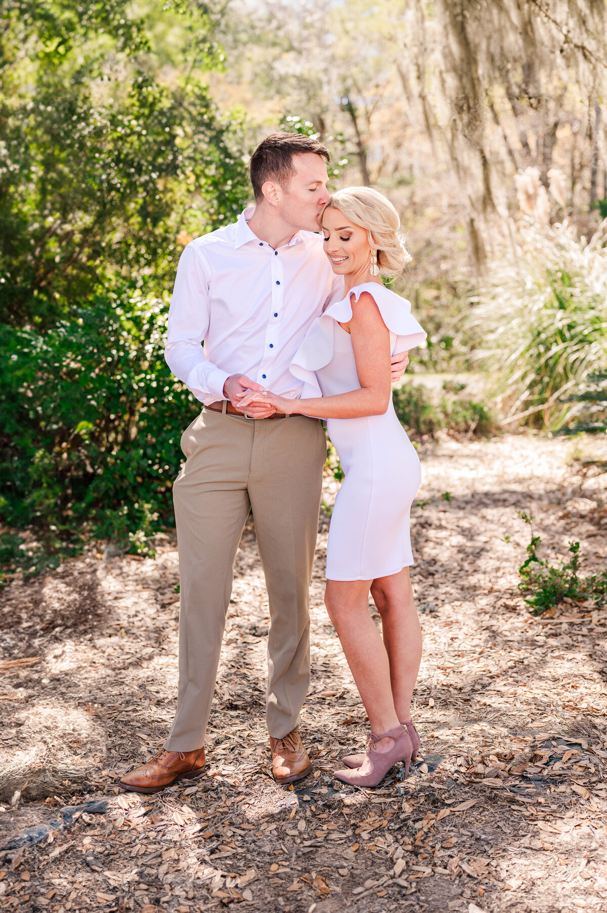 A fiance kissing his blonde bride to be under the Spanish moss in a Raleigh garden by Raleigh wedding photographer, JoLynn Photography