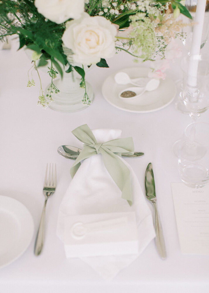 wedding table decoration with white napkins tied with sage green silk ribbon and white roses flower centrepiece