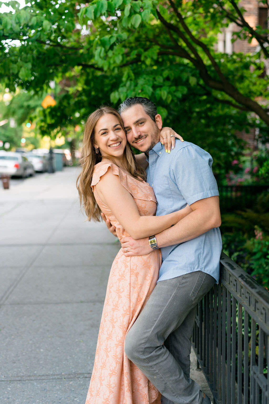 couple hugging and smiling to the side as they lean against a fence