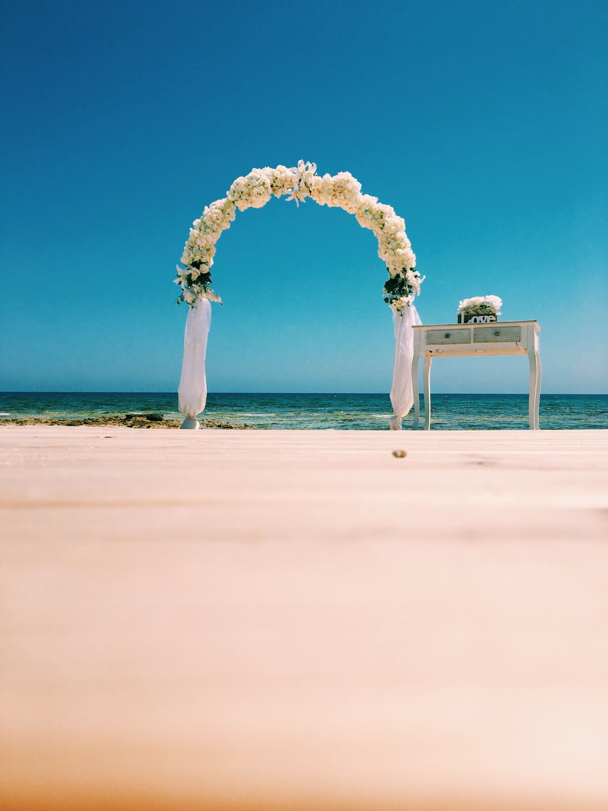 White sand and blue sea with a floral arch and ceremony table