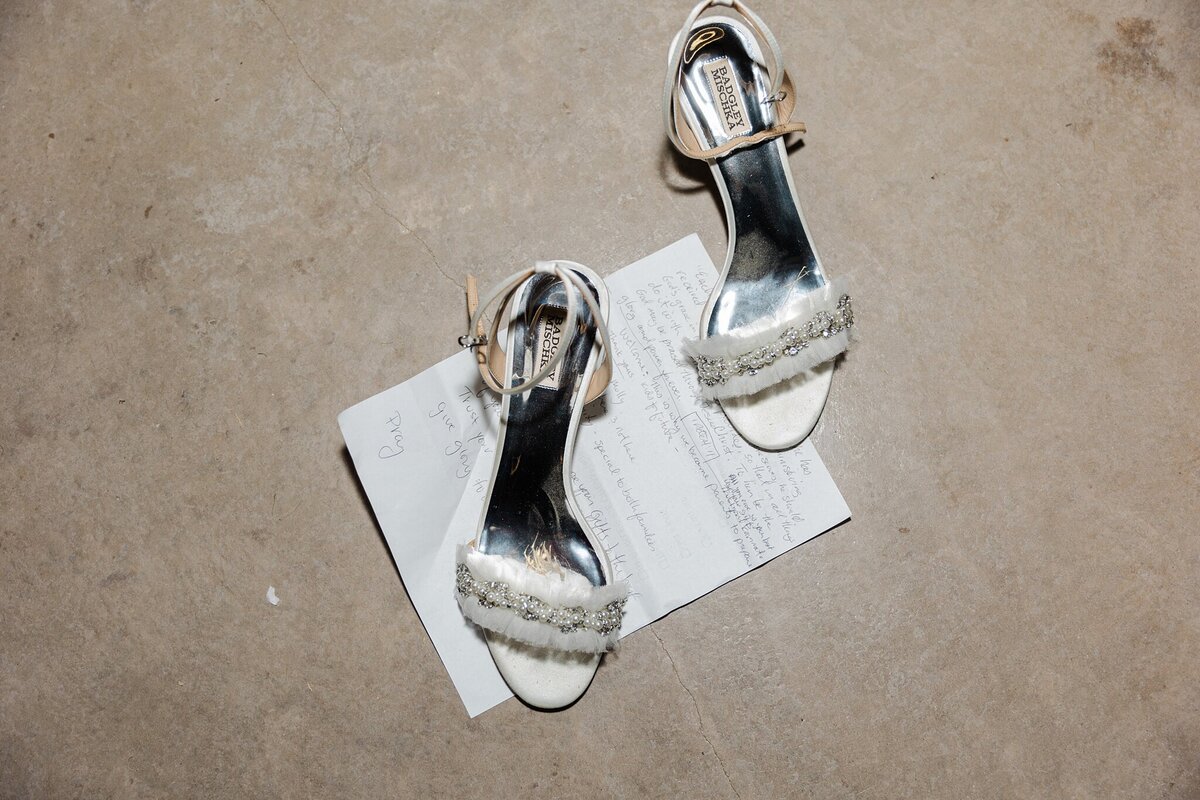 A detail shot of vows and the bride's shoes after having been removed during her wedding reception in Dallas, Texas. The shoes are silver heels, and the vows are handwritten.