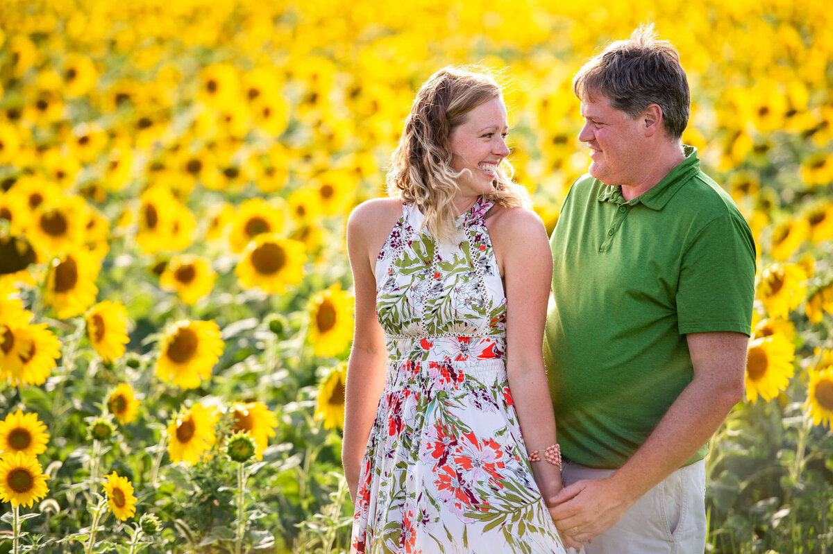 Family Photography in Ottawa of a mom and dad holding hands and smiling in a field of sunflowers at sunset